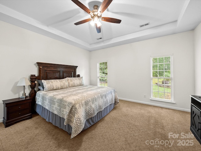 bedroom featuring a raised ceiling, visible vents, light colored carpet, and multiple windows