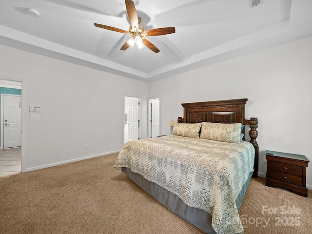 bedroom featuring light carpet, ceiling fan, ensuite bathroom, baseboards, and a raised ceiling