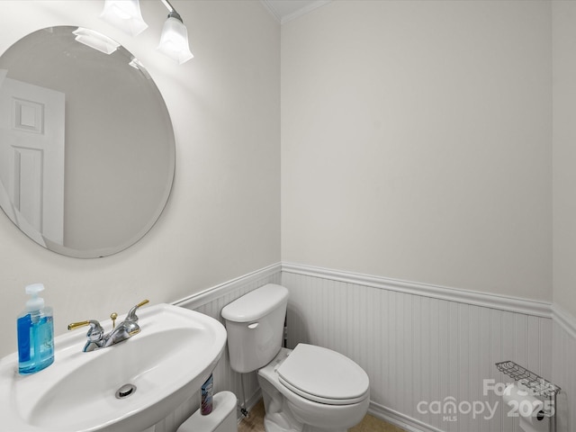 half bathroom with toilet, crown molding, a wainscoted wall, and a sink