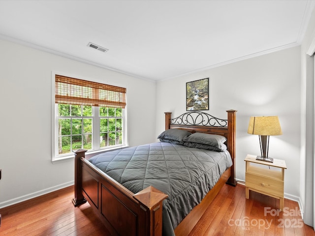 bedroom with crown molding, visible vents, hardwood / wood-style floors, and baseboards