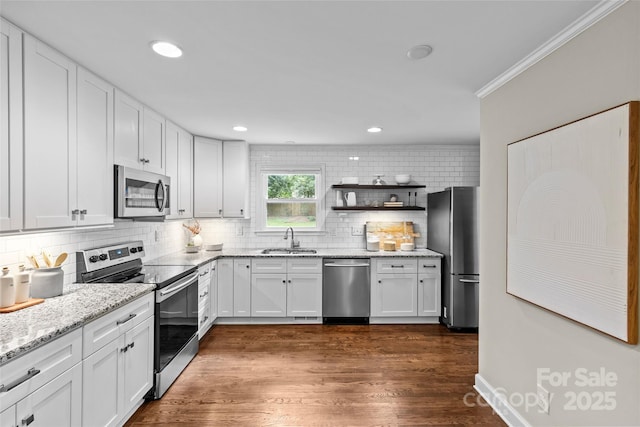 kitchen featuring white cabinets, light stone countertops, appliances with stainless steel finishes, a sink, and decorative backsplash