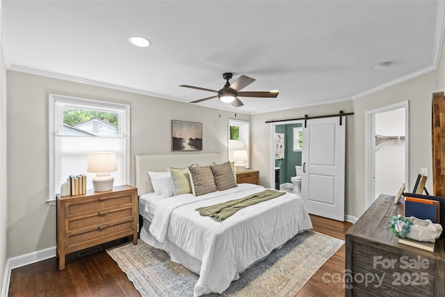 bedroom with crown molding, dark wood-style flooring, baseboards, a walk in closet, and a barn door
