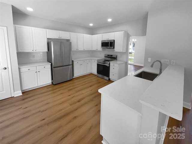 9830 Sandman Ln, Charlotte, NC 28216 - kitchen featuring stainless steel appliances, a peninsula, a sink, light wood-type flooring, and white cabinetry