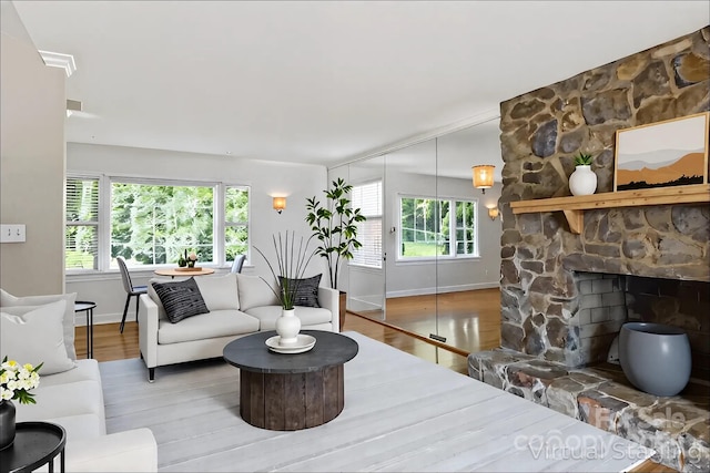 living room with baseboards, a stone fireplace, and wood finished floors