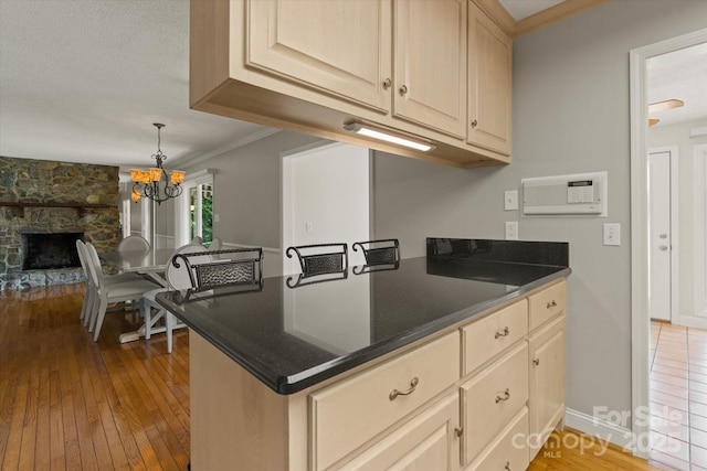 kitchen with crown molding, pendant lighting, a stone fireplace, a chandelier, and hardwood / wood-style flooring
