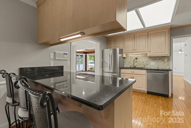 kitchen featuring crown molding, appliances with stainless steel finishes, a sink, light wood finished floors, and a peninsula