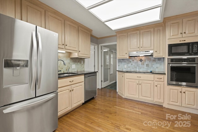 kitchen with under cabinet range hood, stainless steel appliances, decorative backsplash, and a sink