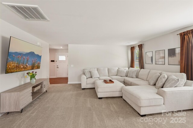 living area featuring visible vents, baseboards, and light carpet