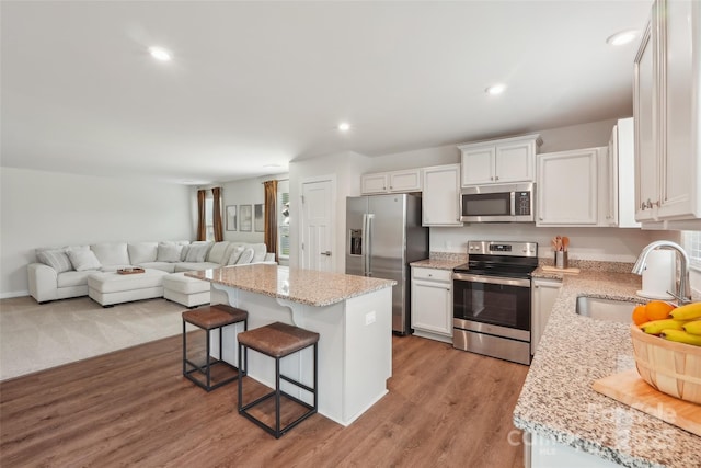 kitchen featuring a sink, a center island, a breakfast bar, white cabinets, and appliances with stainless steel finishes