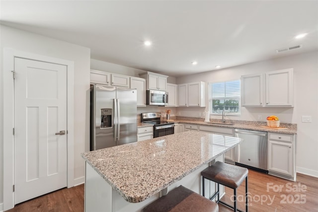 kitchen featuring a sink, stainless steel appliances, a center island, visible vents, and wood finished floors