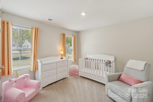 bedroom with visible vents, a nursery area, and light colored carpet