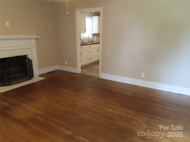 unfurnished living room featuring baseboards, a sink, a fireplace with flush hearth, and dark wood-type flooring