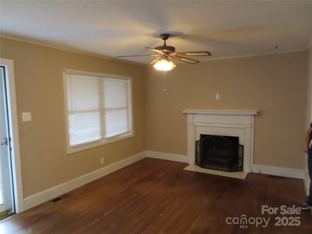 unfurnished living room with dark wood finished floors, visible vents, a ceiling fan, a fireplace with flush hearth, and crown molding