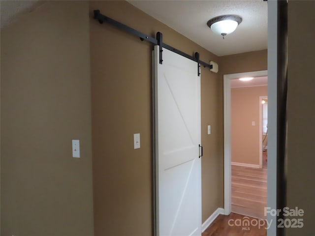 hall with wood finished floors, a barn door, and baseboards