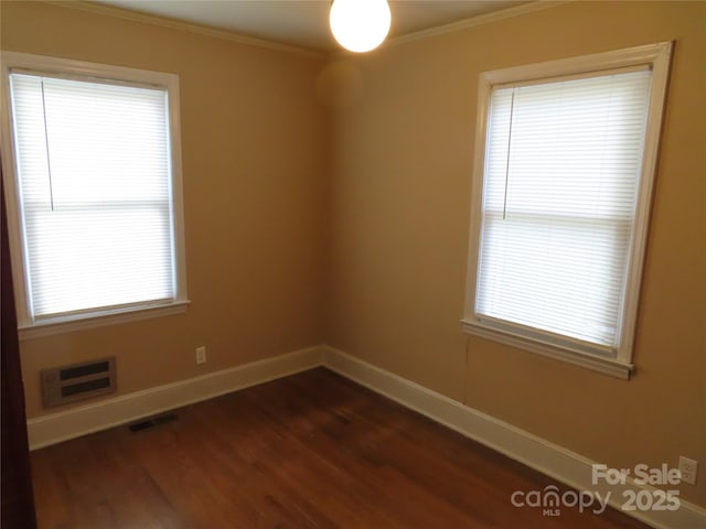 empty room featuring dark wood-style floors, baseboards, ornamental molding, and plenty of natural light