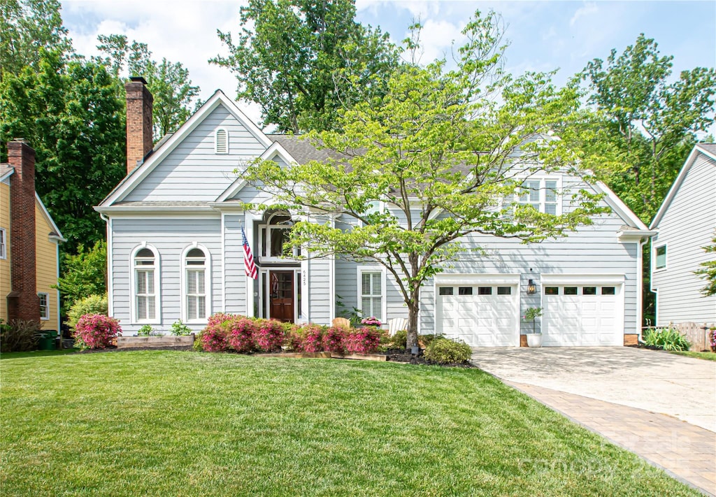 view of front facade featuring a chimney, a front lawn, concrete driveway, and an attached garage