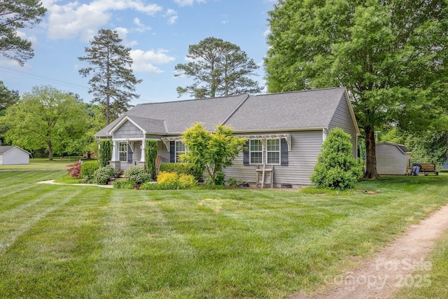 ranch-style house with roof with shingles, a front lawn, and a storage shed