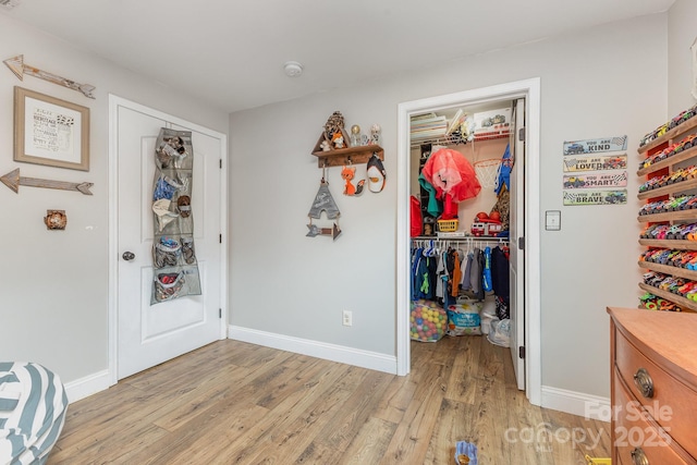 bedroom featuring a closet, light wood-style flooring, a walk in closet, and baseboards