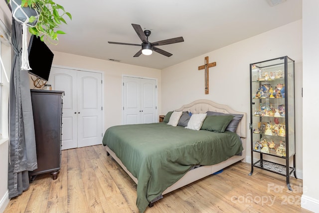 bedroom with light wood-style floors, two closets, a ceiling fan, baseboards, and visible vents