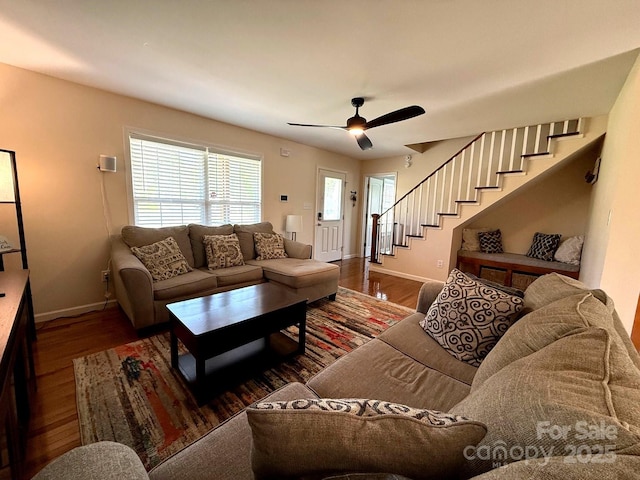 living area featuring baseboards, a ceiling fan, wood finished floors, and stairway