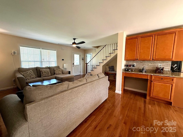 living room featuring baseboards, ceiling fan, stairs, and dark wood-style floors