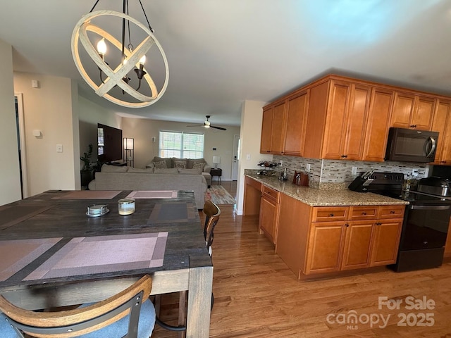kitchen featuring light stone countertops, brown cabinetry, light wood finished floors, and black appliances