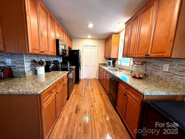 kitchen with a sink, light wood-style floors, brown cabinetry, backsplash, and black appliances