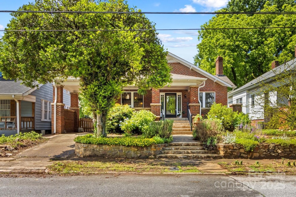 view of property hidden behind natural elements with brick siding, a chimney, and covered porch