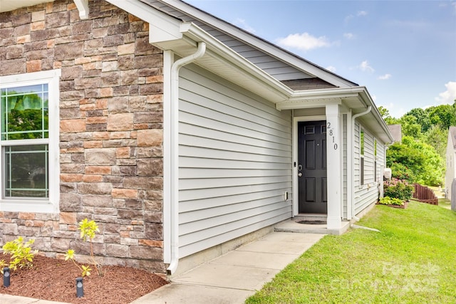 view of exterior entry featuring a lawn and stone siding