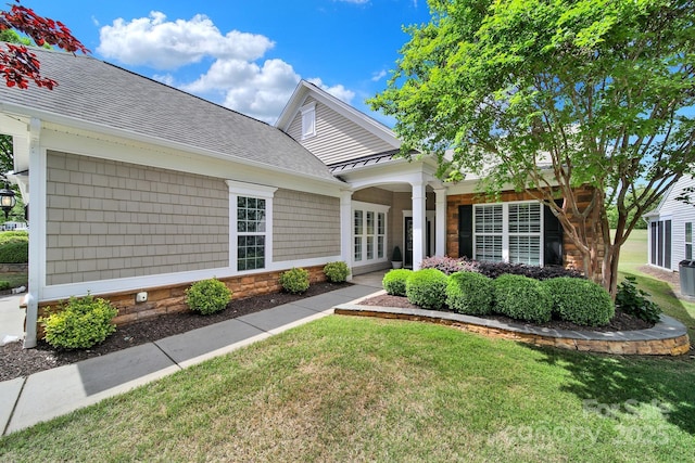 view of front of home featuring a front lawn, stone siding, and a shingled roof