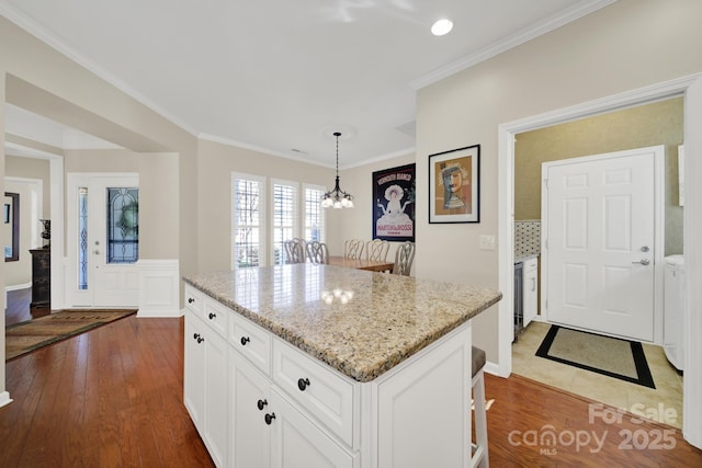 kitchen featuring a center island, white cabinets, crown molding, and light stone counters