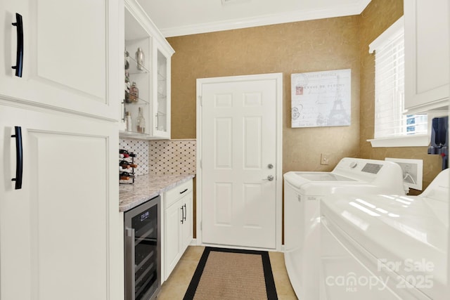 laundry room with a bar, light tile patterned floors, washing machine and dryer, ornamental molding, and beverage cooler