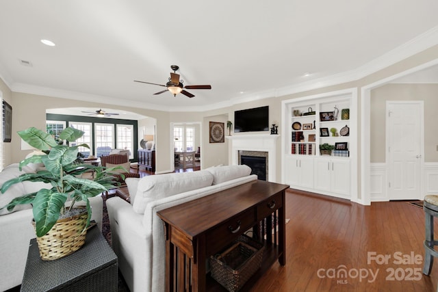 living area with visible vents, ceiling fan, a glass covered fireplace, dark wood-style flooring, and ornamental molding
