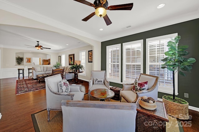 living area with crown molding, visible vents, arched walkways, wood finished floors, and a ceiling fan