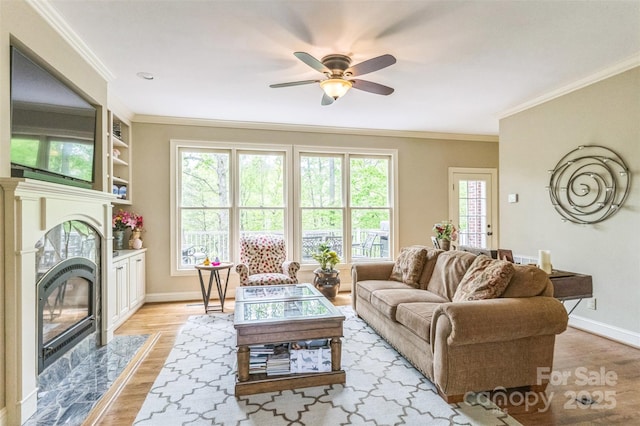 living room with a ceiling fan, crown molding, baseboards, light wood finished floors, and a premium fireplace