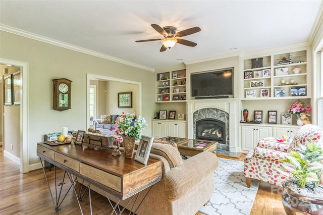 living room featuring ceiling fan, built in shelves, wood finished floors, a high end fireplace, and ornamental molding