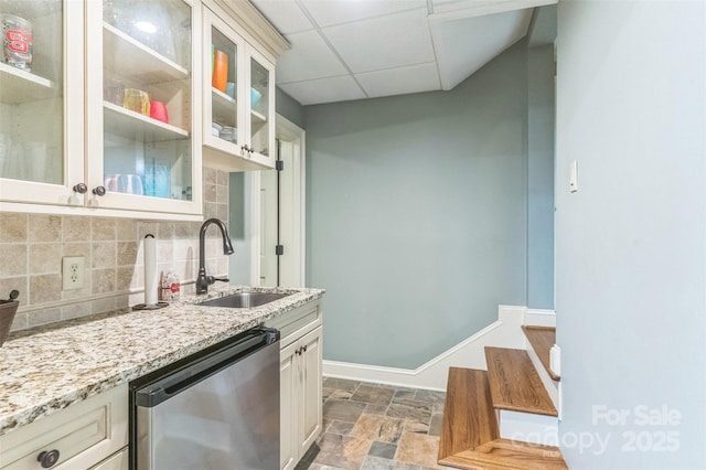 kitchen featuring light stone countertops, dishwashing machine, a drop ceiling, a sink, and stone finish flooring