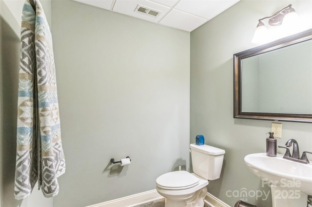 bathroom featuring a sink, toilet, a paneled ceiling, baseboards, and visible vents