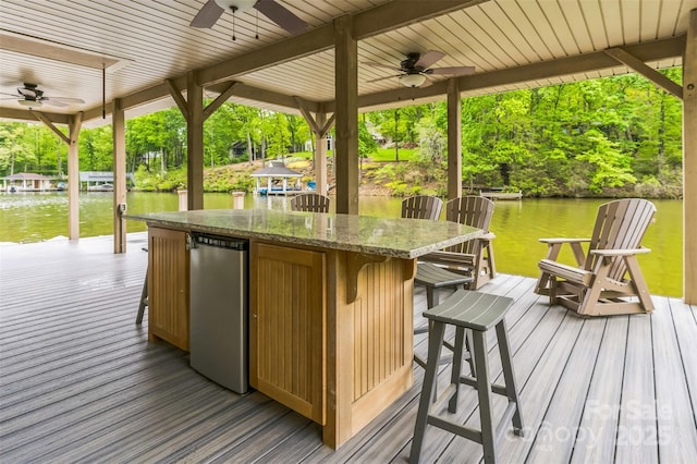 wooden terrace with a water view, outdoor dry bar, and ceiling fan