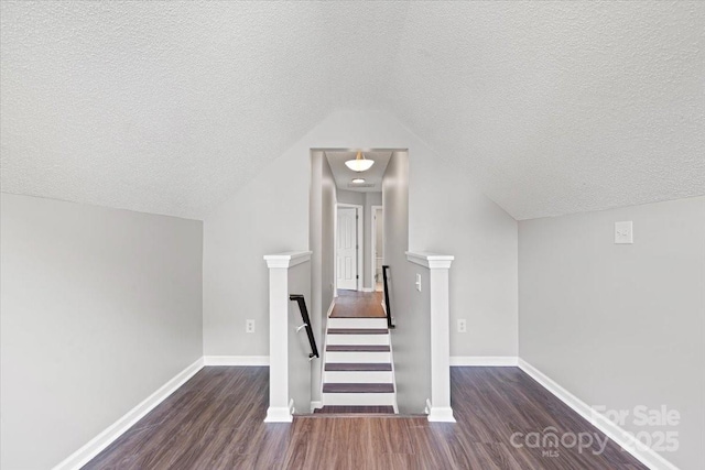 stairs featuring lofted ceiling, a textured ceiling, wood finished floors, and baseboards