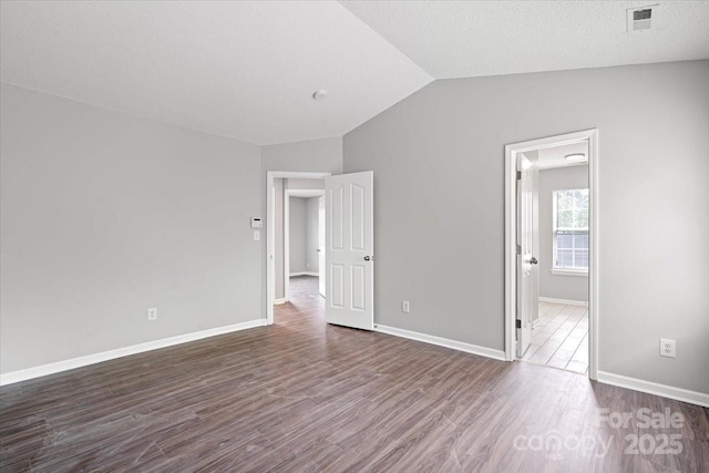 unfurnished bedroom with dark wood-type flooring, visible vents, vaulted ceiling, and baseboards