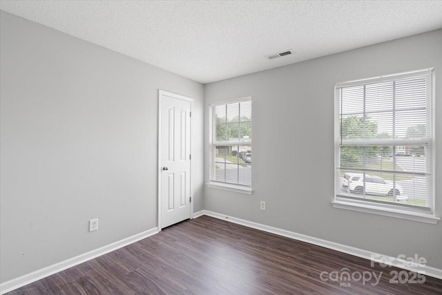 unfurnished room featuring dark wood finished floors, baseboards, visible vents, and a textured ceiling