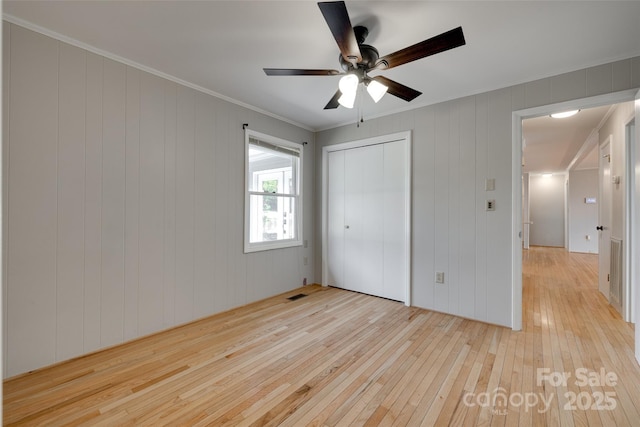 unfurnished bedroom with a closet, ornamental molding, visible vents, ceiling fan, and light wood-style flooring