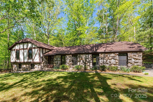 view of front of house featuring a shingled roof, stone siding, and a front lawn