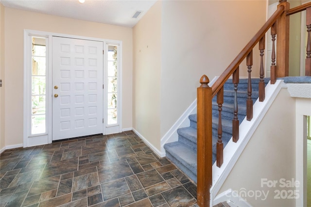 foyer featuring stairway, stone finish floor, baseboards, and visible vents