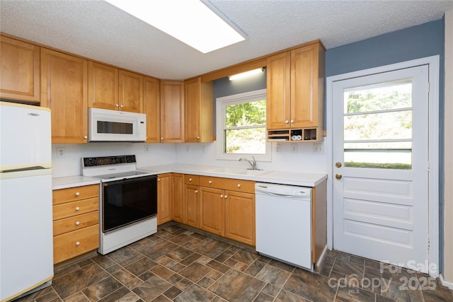 kitchen with stone finish flooring, a textured ceiling, light countertops, a sink, and white appliances