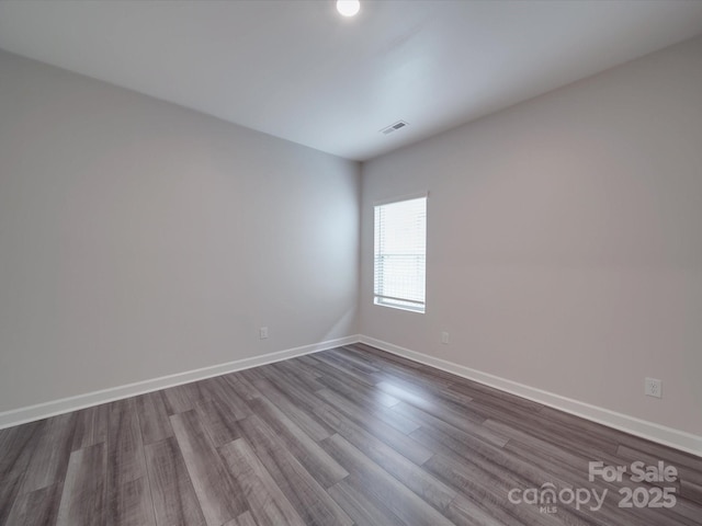 spare room featuring baseboards, visible vents, and dark wood-type flooring