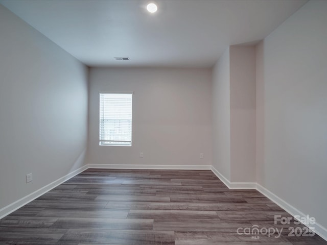 unfurnished room featuring visible vents, dark wood-style flooring, and baseboards