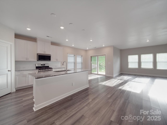 kitchen with wood finished floors, a center island with sink, white cabinetry, a sink, and appliances with stainless steel finishes