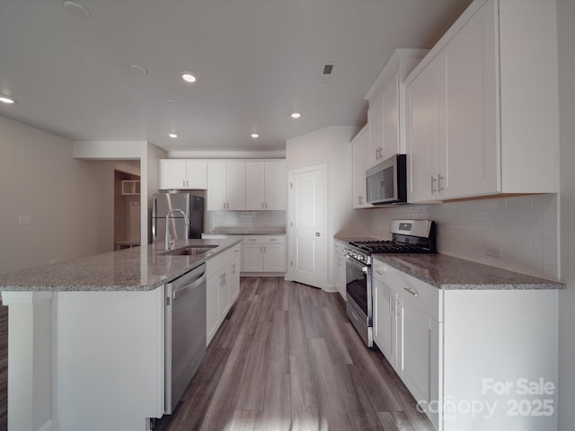 kitchen featuring appliances with stainless steel finishes, tasteful backsplash, wood finished floors, a sink, and recessed lighting